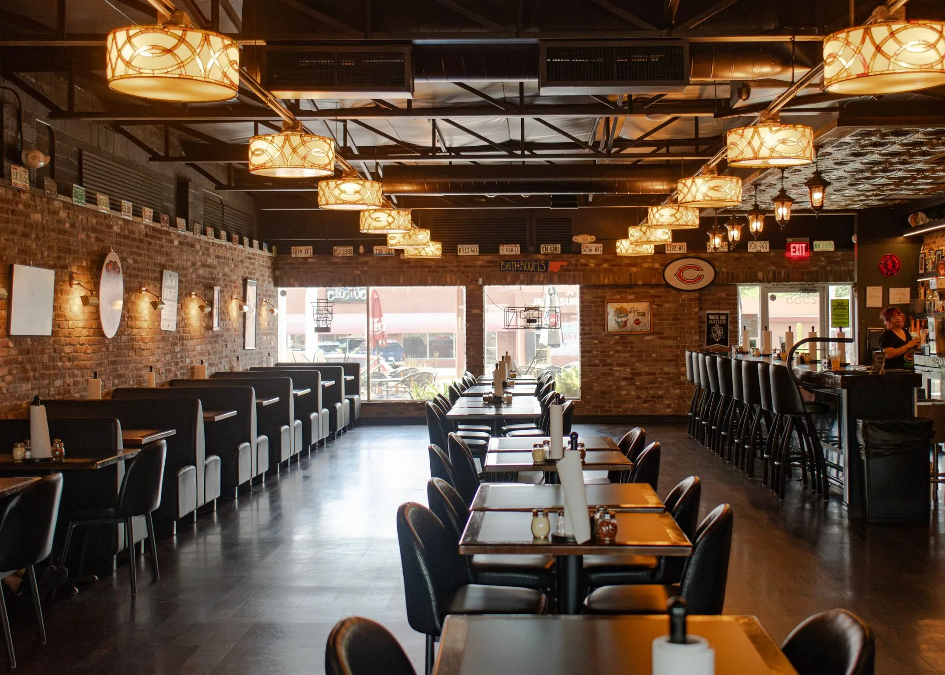 The dining room looking towards the front windows, a row of booths along one wall and tables set down the middle under pendant lights