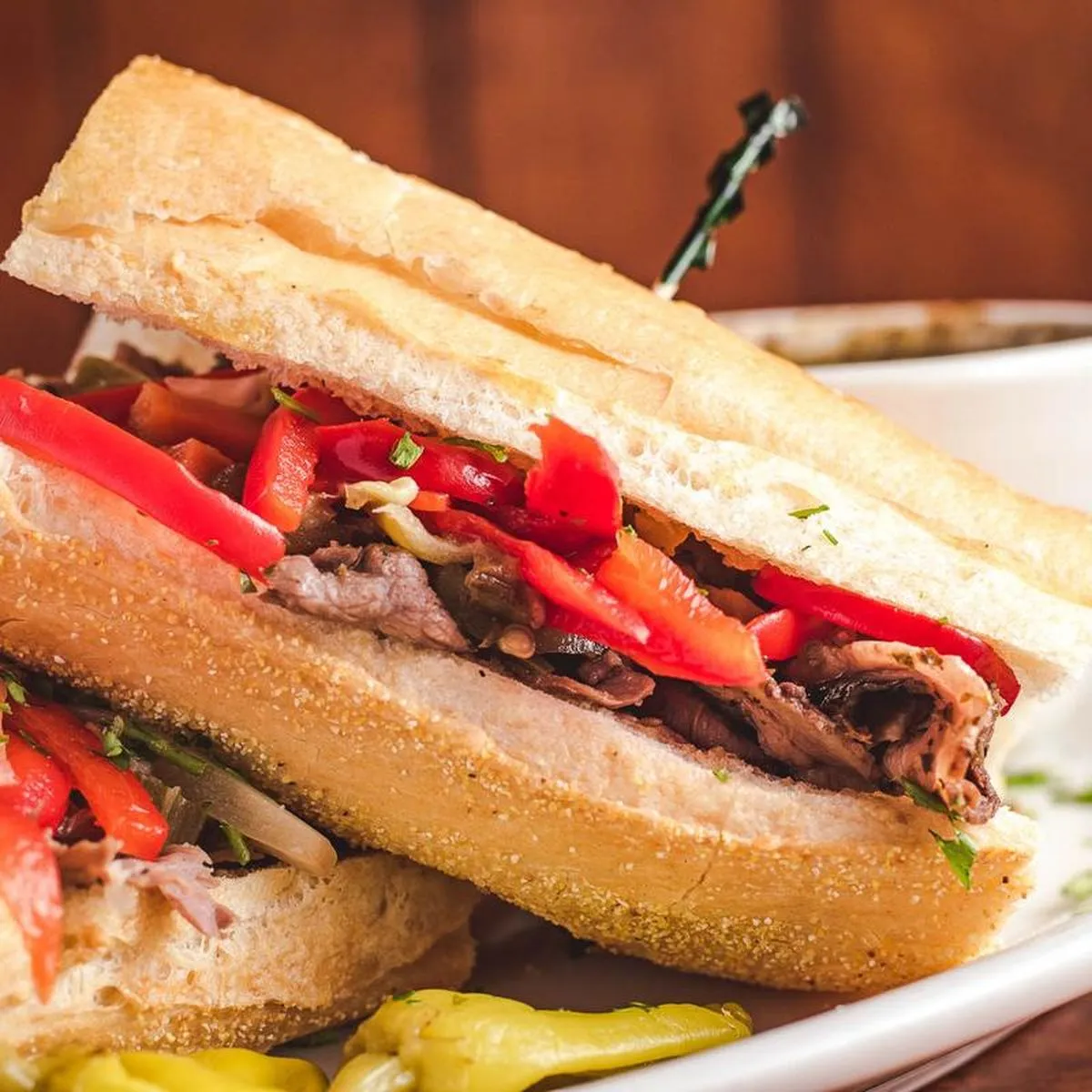 Italian beef sandwich on French bread, cut in half and stacked, with red peppers and pepperoncini