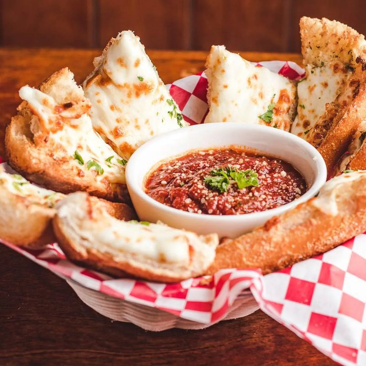 Basket of cheese-topped garlic bread with a ramekin of marinara to dip