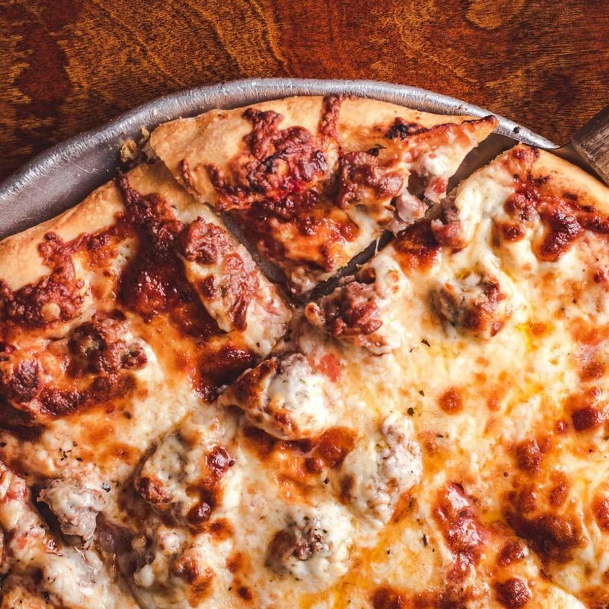 Close-up of a sliced thin crust sausage pizza on a steel pan