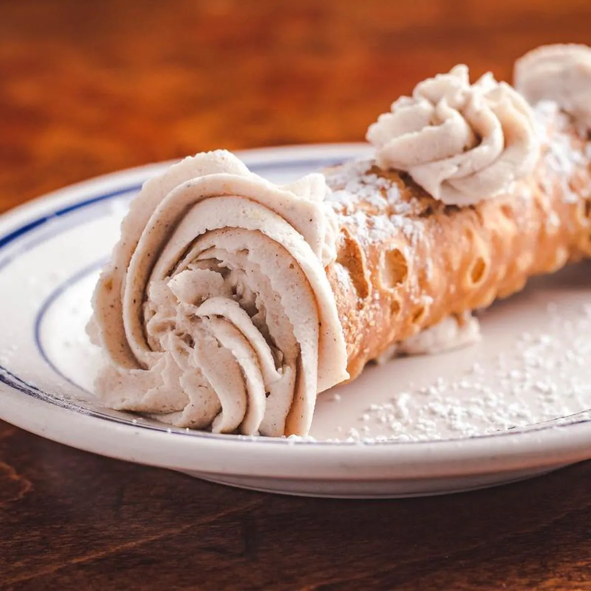 Cannoli on a plate, cream piped at both ends and dusted with powdered sugar