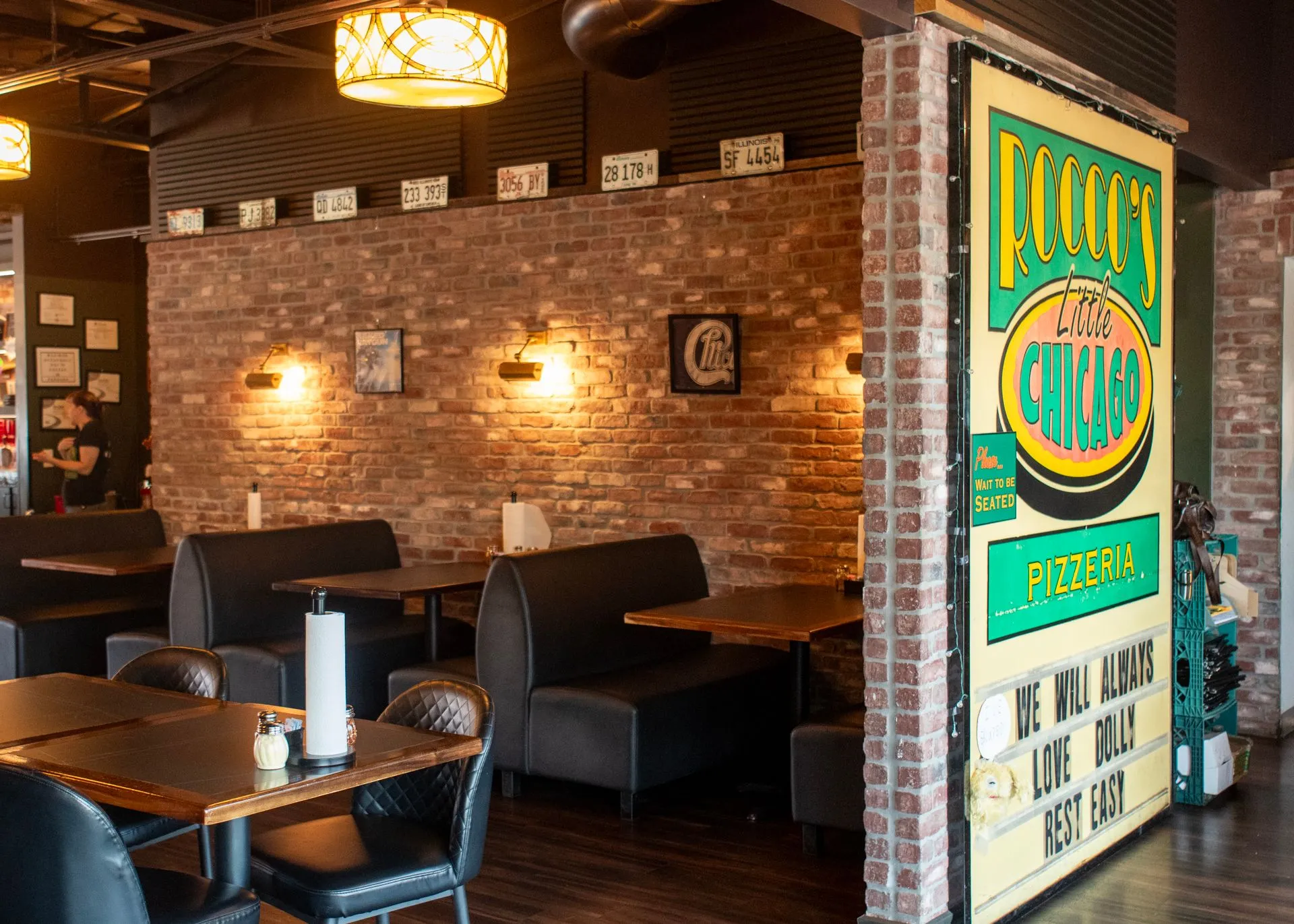 Booths beside the brick pillar carrying the painted Rocco's Little Chicago Pizzeria sign