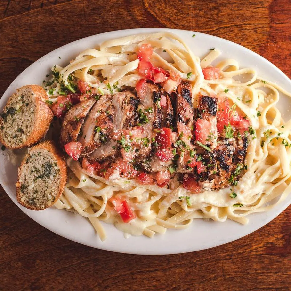 Fettuccine alfredo with grilled chicken and diced tomato, garlic bread on the plate