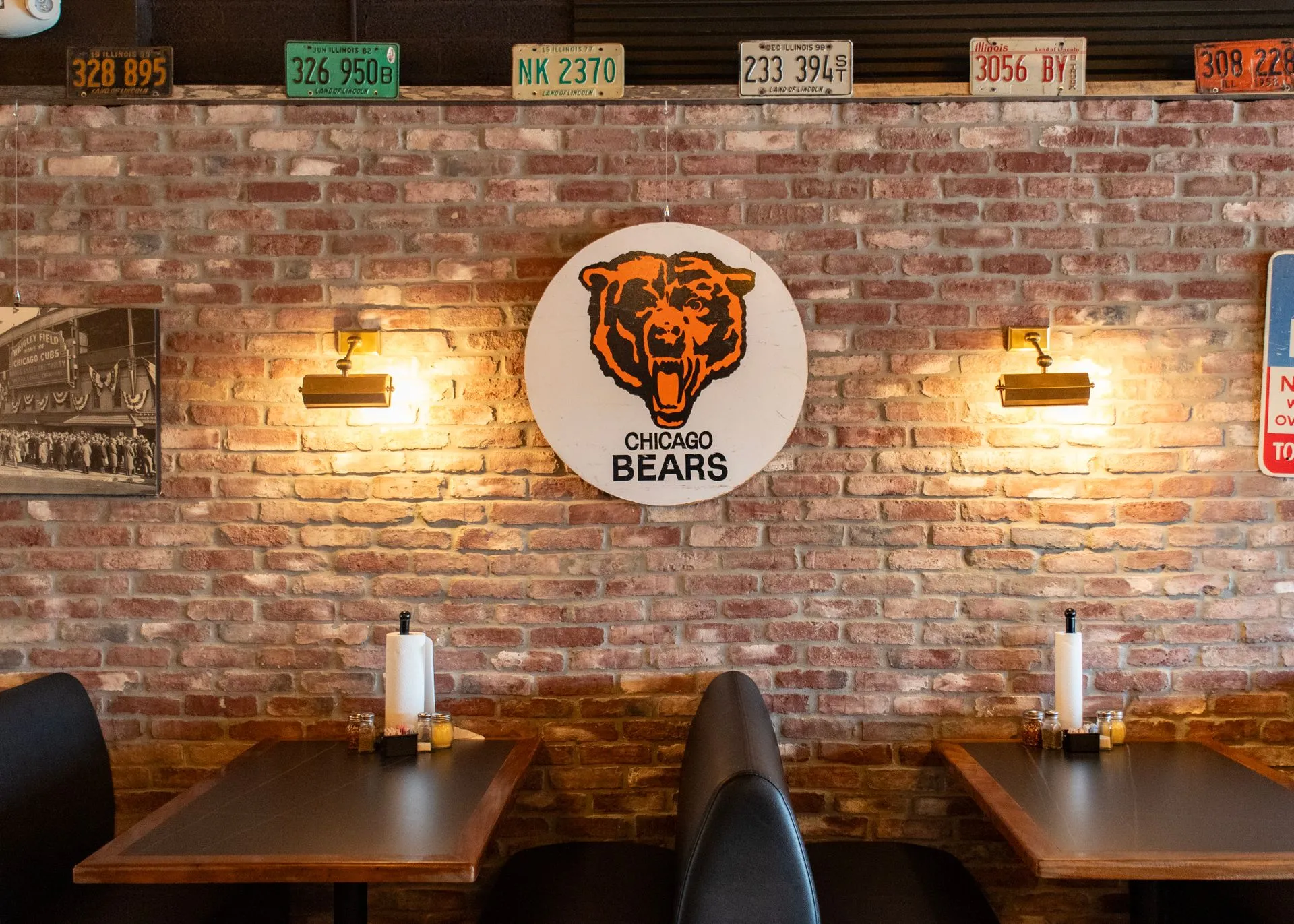 Two tables against the exposed brick wall under a Chicago Bears sign, with vintage licence plates lining the top of the wall